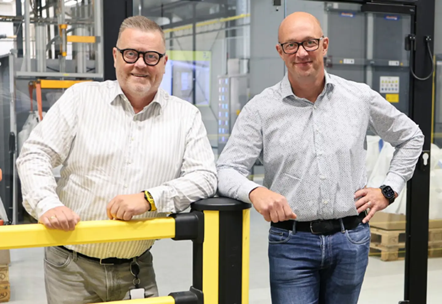 Stefan and Johan Axelsson, owners of Axelent, standing in suits, relaxed against a yellow protection bar