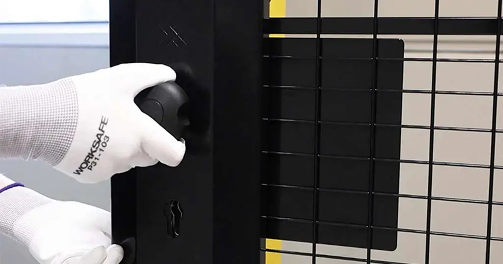 黒いメッシュパネルに取り付けられたシリンダー式パニックリリースを手に持つ手